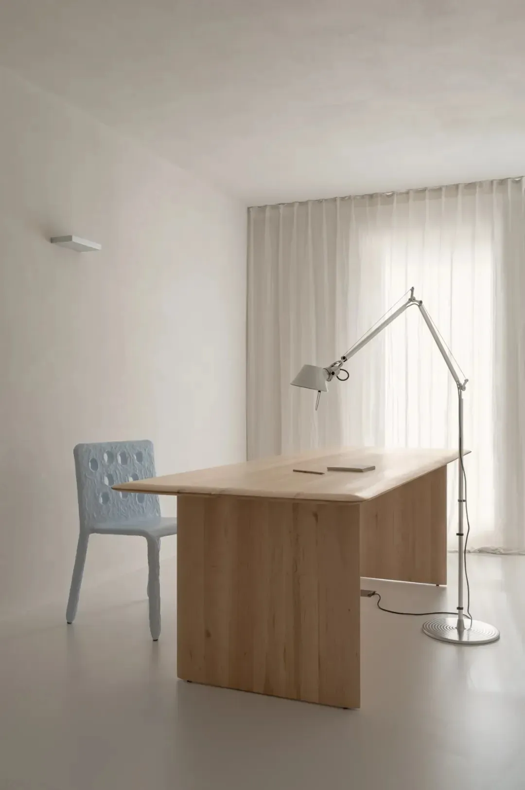 A minimalist home office featuring a wooden desk and blue woven chair with a floor lamp