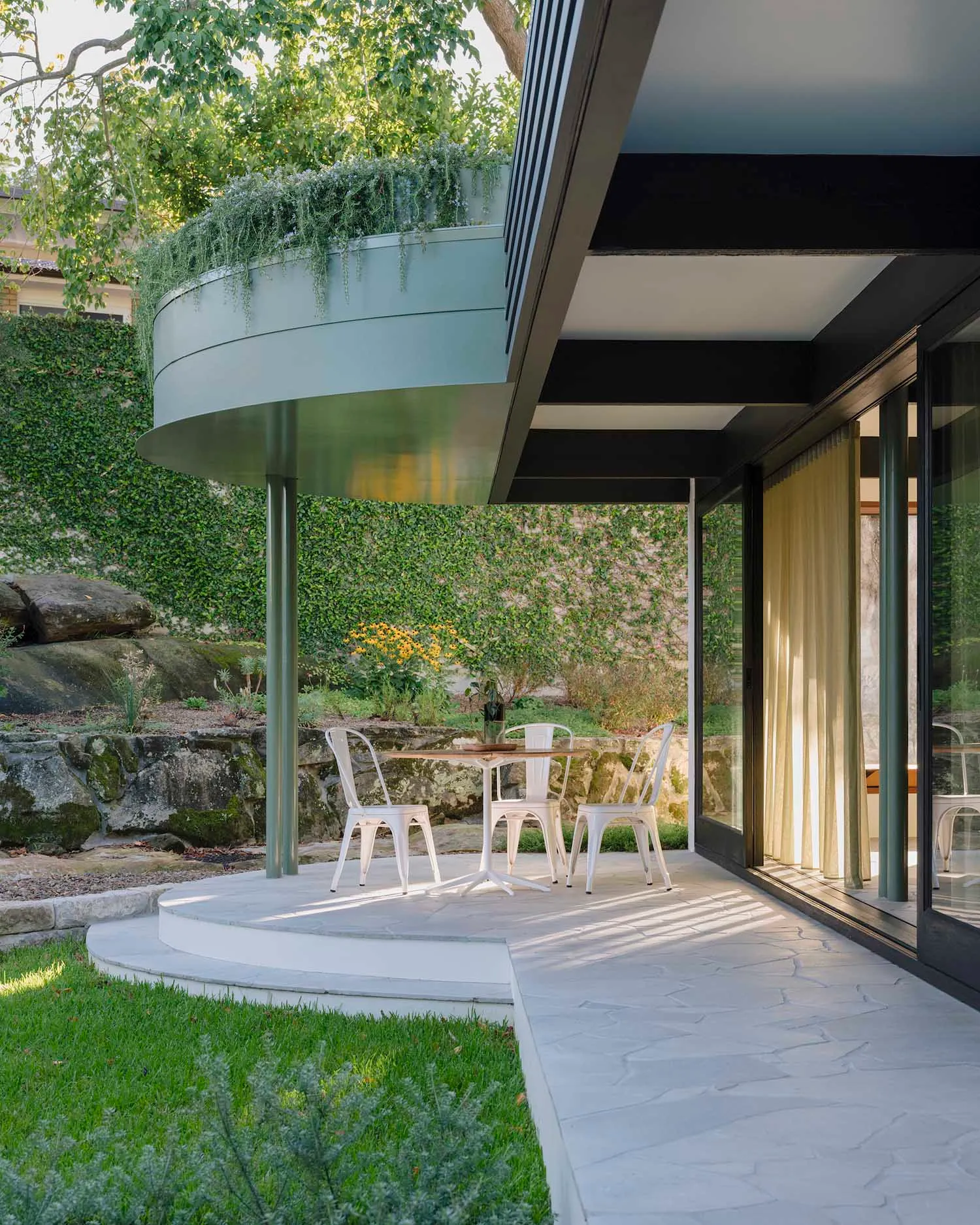 A modern minimalist patio made of concrete and metal with white chairs and a table.