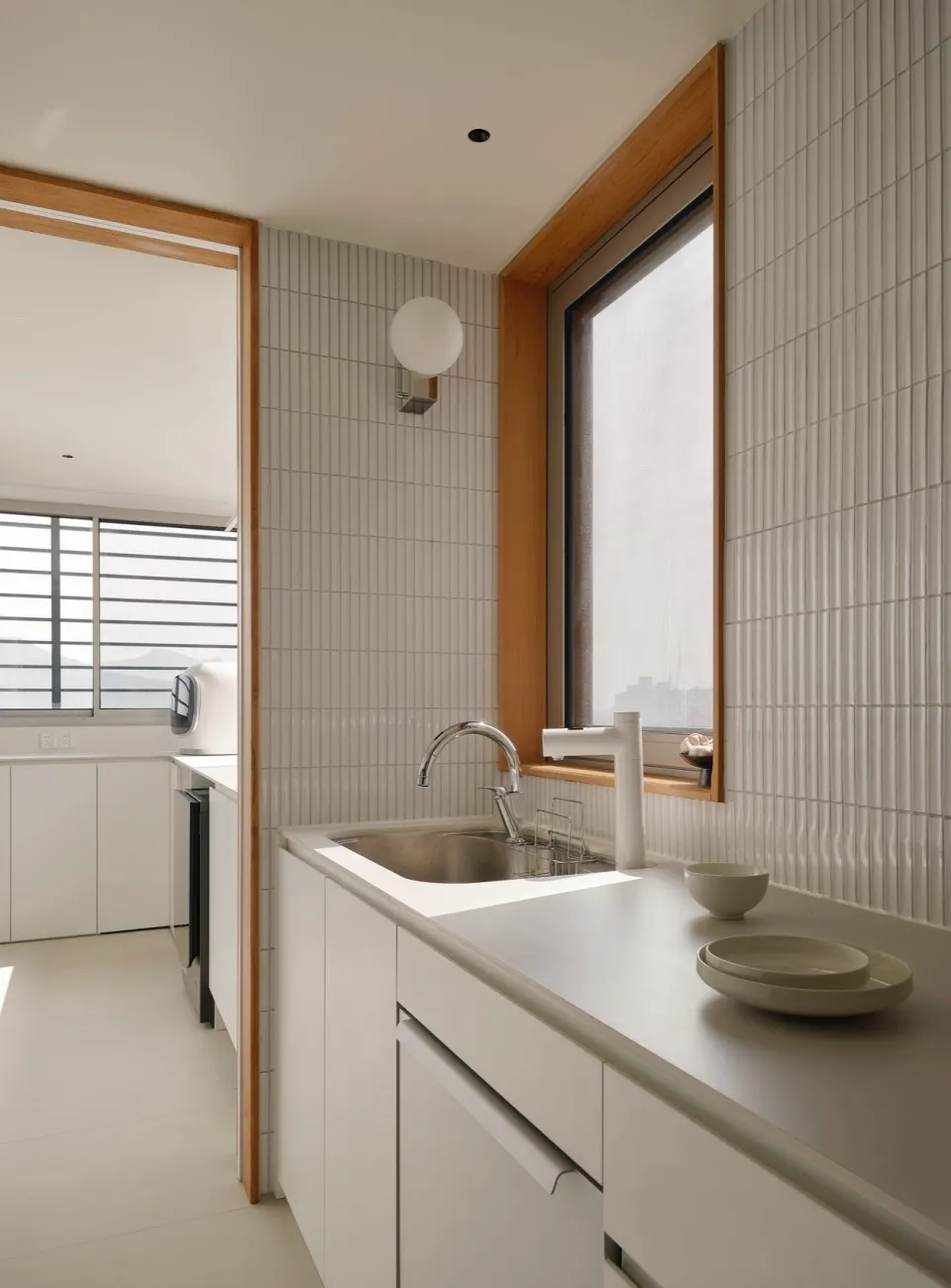 Modern kitchen with white tiled countertops and backsplash, featuring a stainless steel sink and minimalist design.