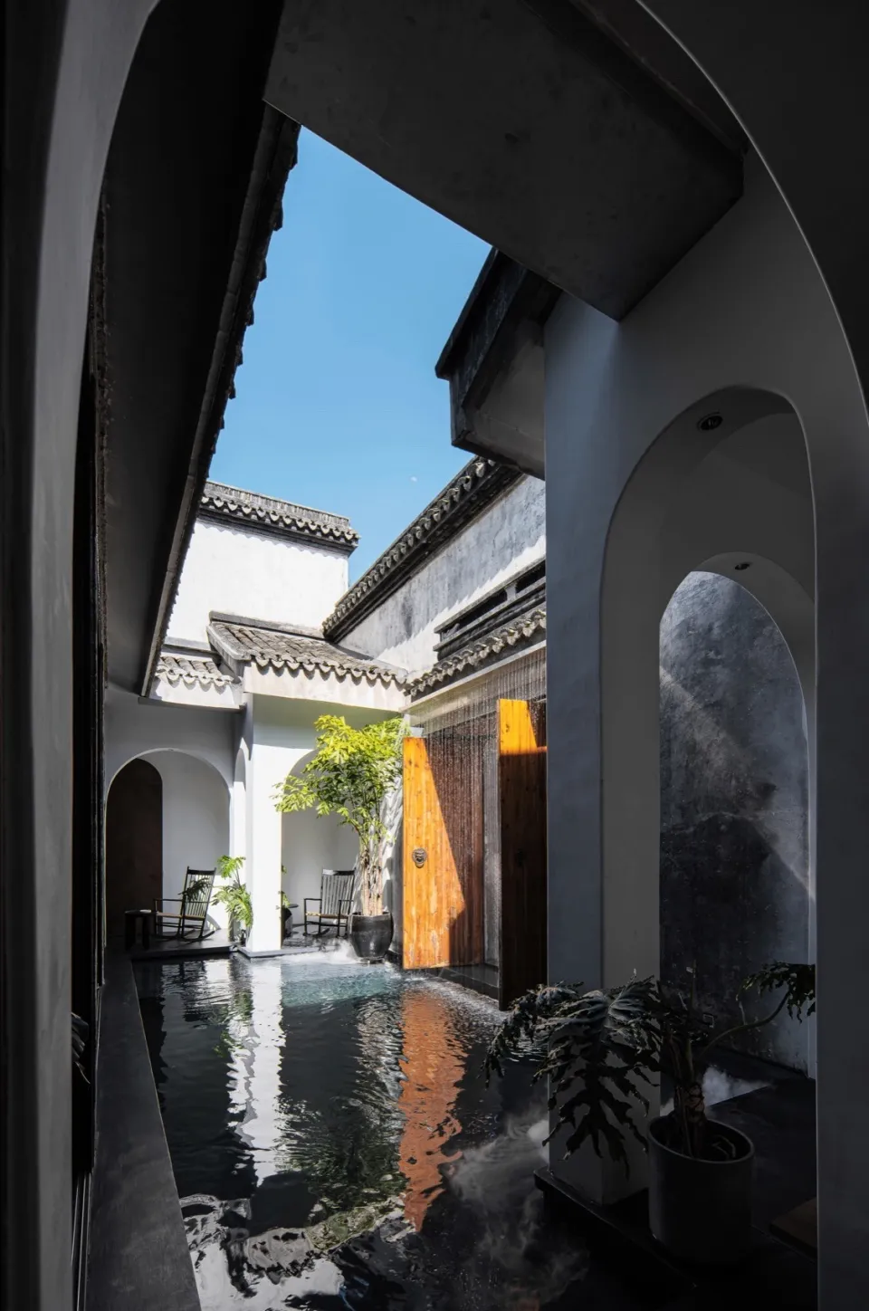極簡住宅走廊,混凝土牆面與地板,拱形門通往庭院,庭院內有池塘