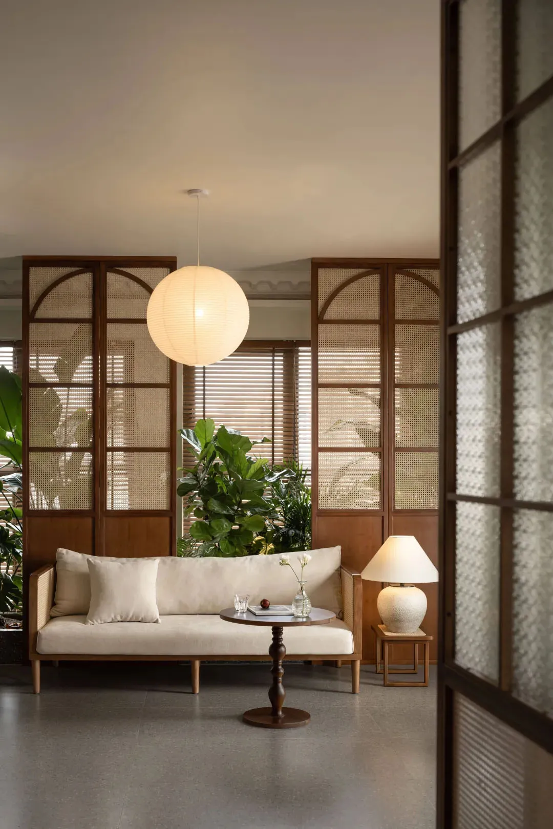 Minimalist living room with beige sofa, wood flooring, and large potted plants.
