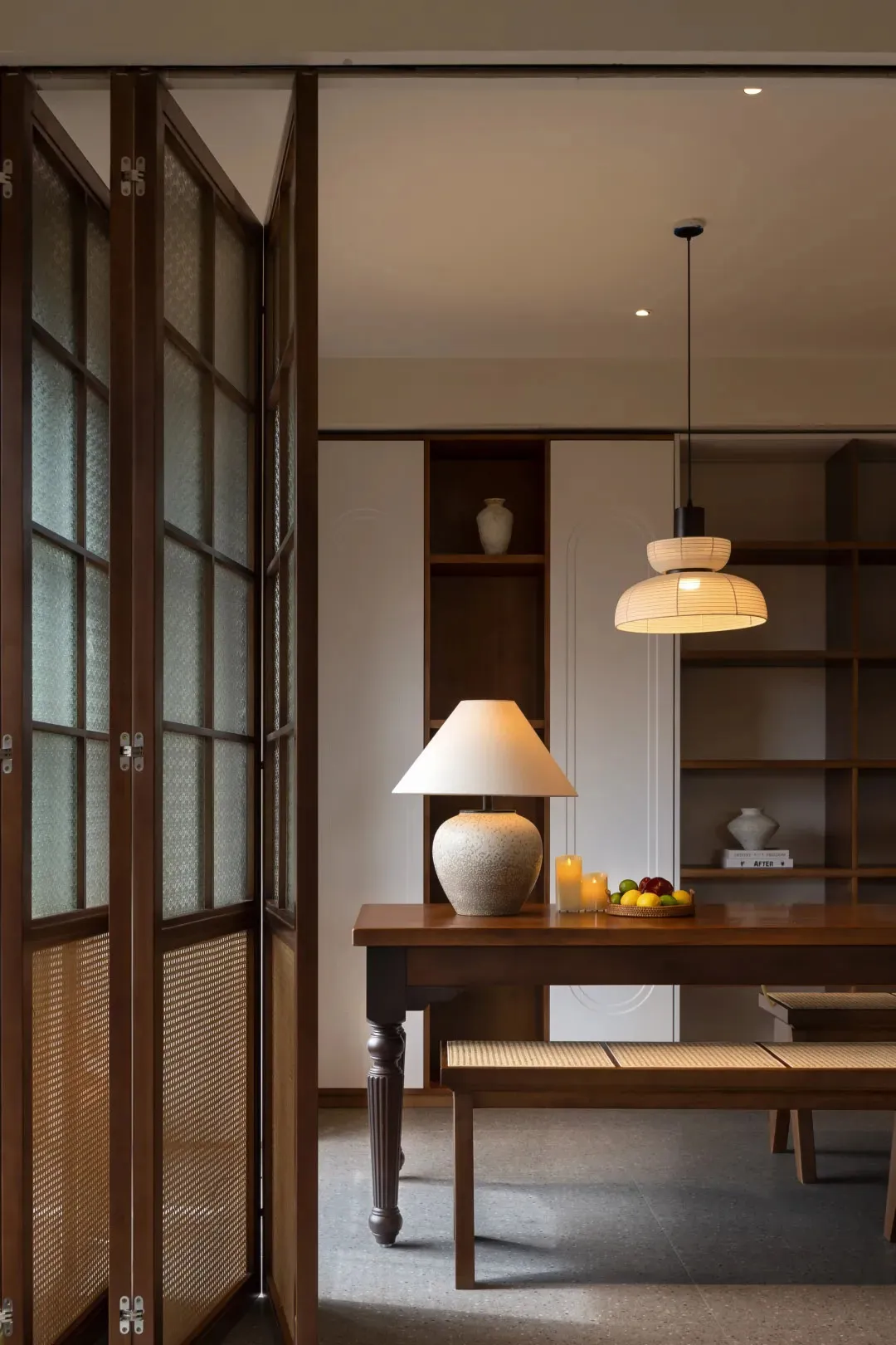A modern dining room featuring wooden furniture, a table lamp, and a fruit basket.