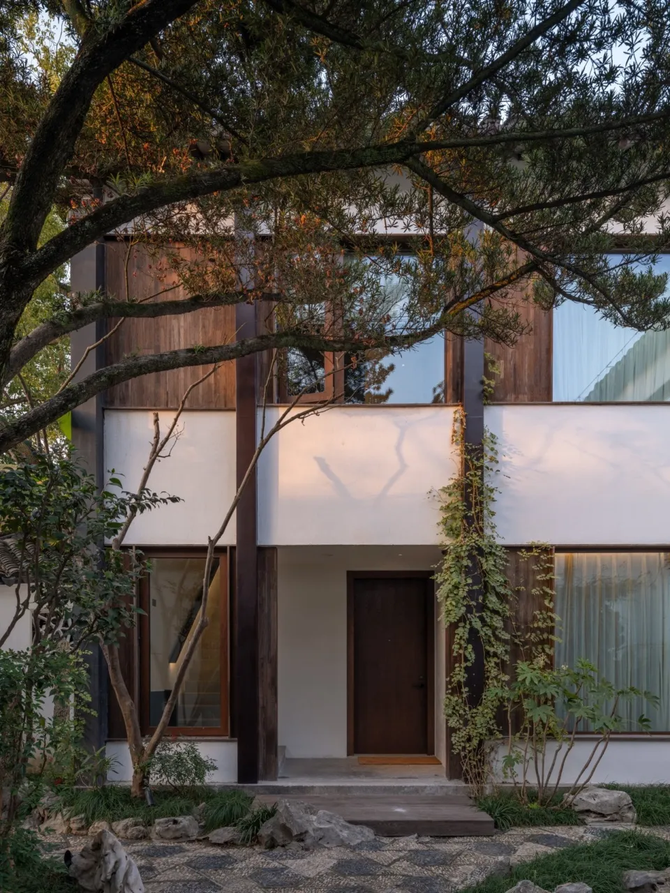 A minimalist residential home with wooden exterior, glass windows, and concrete features.