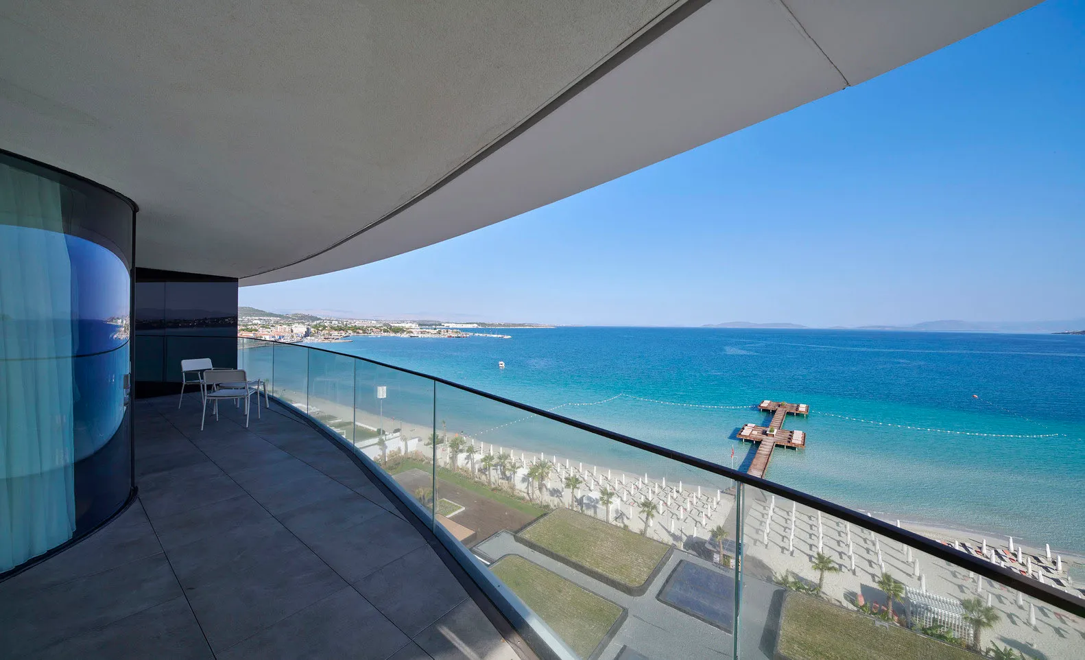 Modern, minimalist apartment balcony overlooking the ocean with clear blue skies and a clear view of the beach.