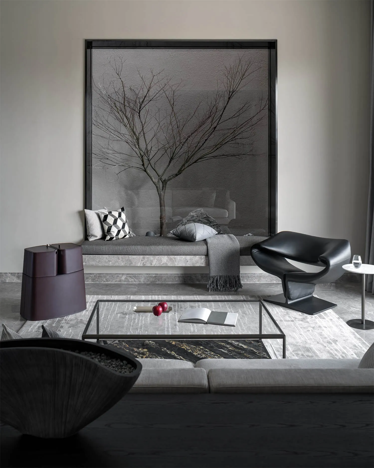 A modern interior design featuring a concrete bench with glass inserts, a black leather armchair, and a glass table.