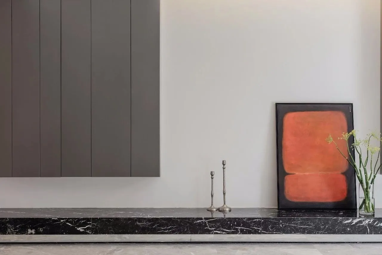 A modern interior scene featuring sleek, dark cabinets, a black marble shelf, and a framed piece of contemporary art with vib