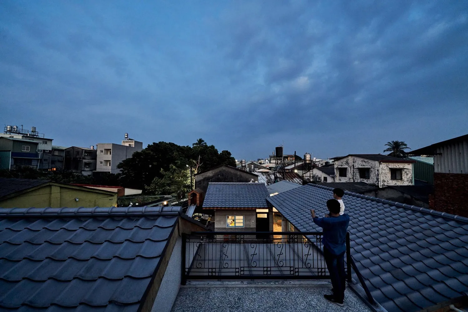 兩人站在屋頂上,背景是住宅建築的瓦片屋頂,呈現黃昏氛圍。
