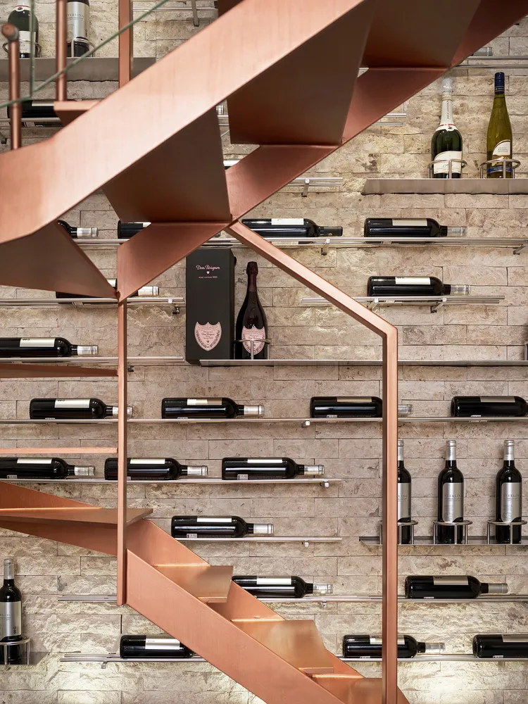 A metal staircase with wine bottles displayed on shelves in a wine-themed interior design setting.