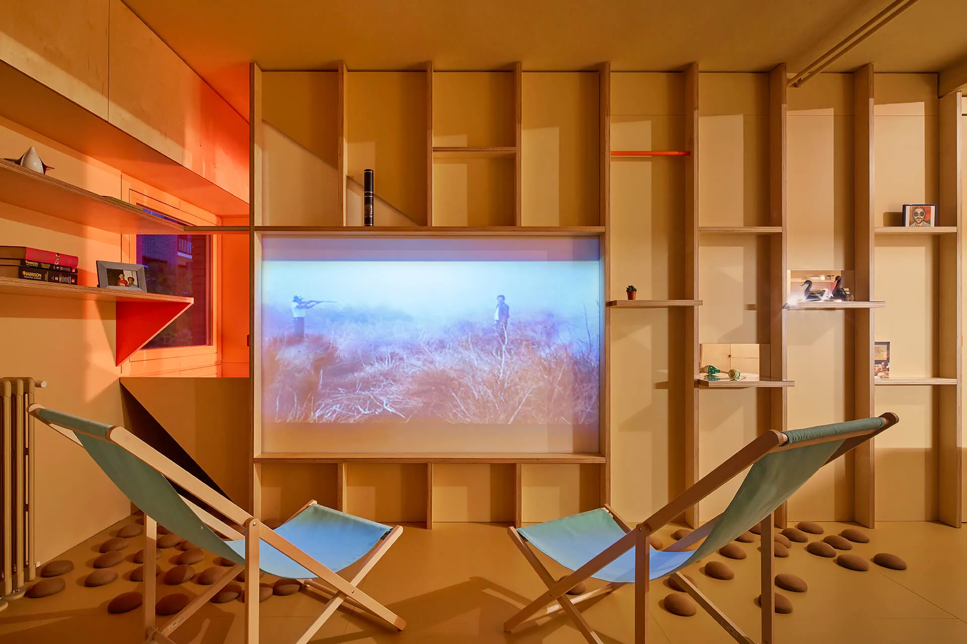 Minimalist entertainment room with wooden shelves and a projected image of a person in the grass.