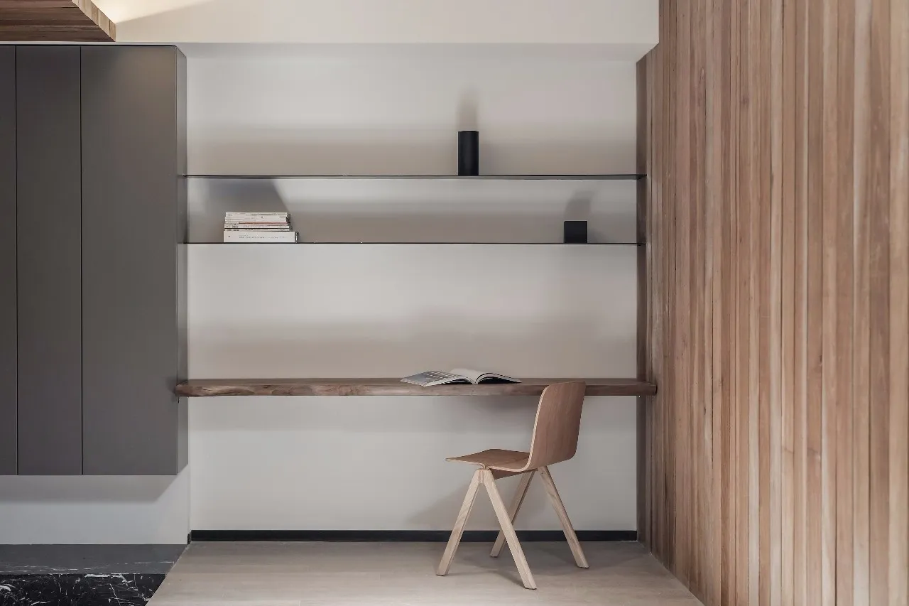 A minimalist interior design featuring a walnut wood desk with books and a chair.