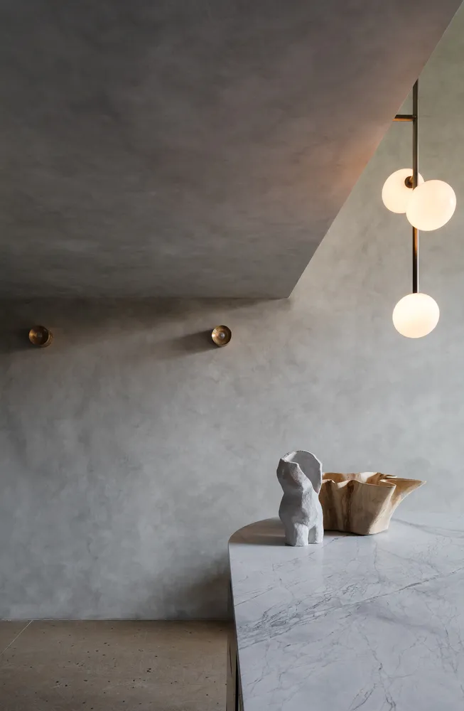 A minimalist living room with concrete walls, marble table, and abstract sculptures.
