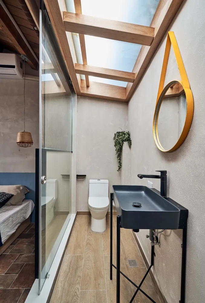 A modern bathroom with concrete walls, a glass shower enclosure, and a black sink with a yellow mirror.