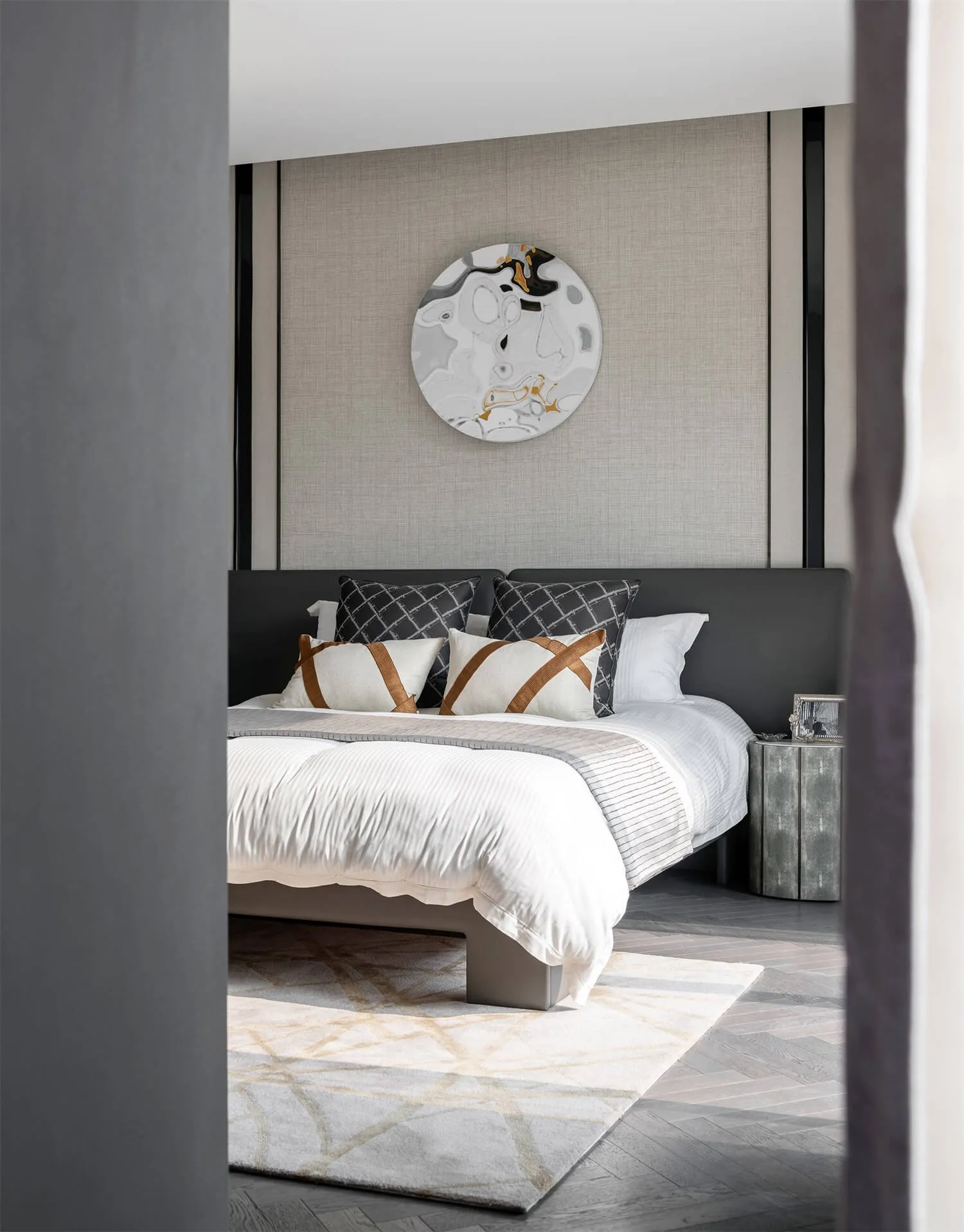 Modern bedroom featuring a bed with a fabric headboard, metallic nightstand, and abstract wall art.