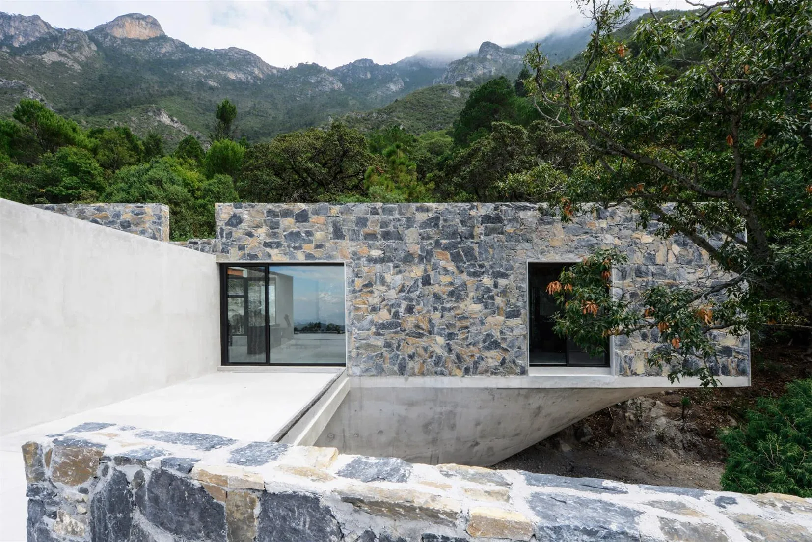 Modern exterior of a mountain residence featuring stone and concrete materials.