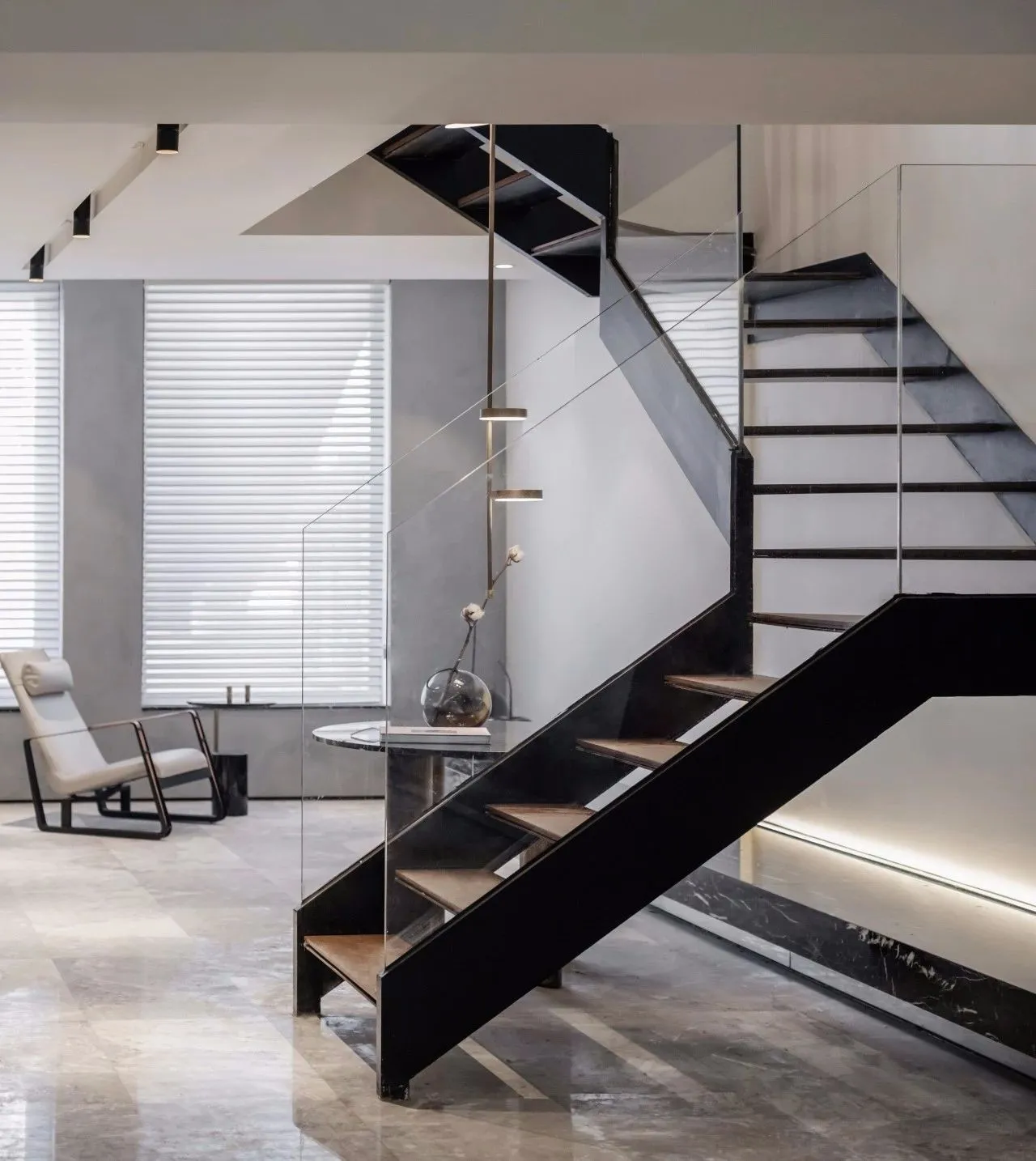 Industrial-style living room featuring modern metal staircase, glass wall, and marble flooring