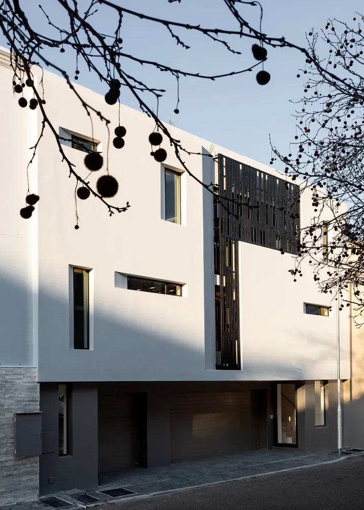 A modern residential building with concrete facade, black metal accents, and large windows.