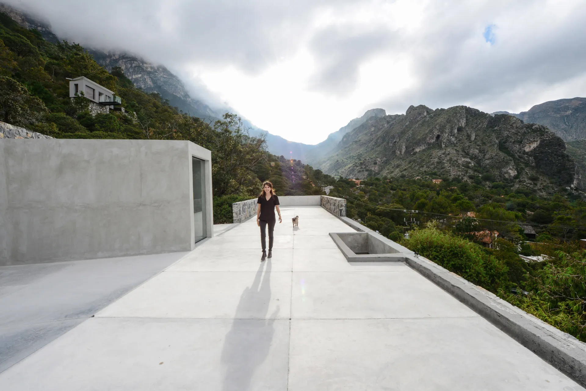 A woman walking her dog on a modern rooftop with concrete flooring and a mountainous landscape in the background.