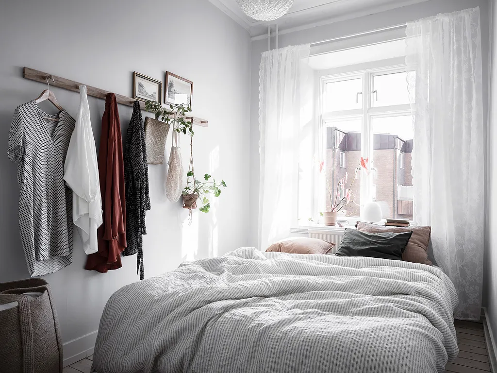 A minimalist bedroom with hanging textiles and a window with a lace curtain.