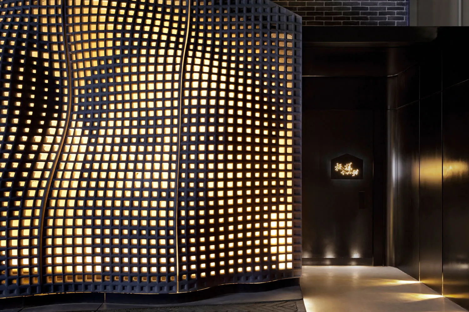 Modern entrance illuminated by a metallic grid wall