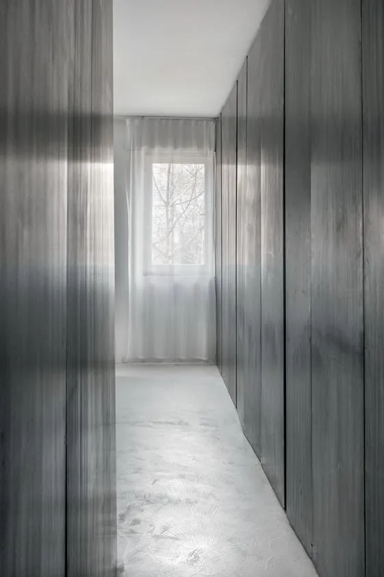 A minimalist residential corridor with metal panels, glass window, and white flooring.