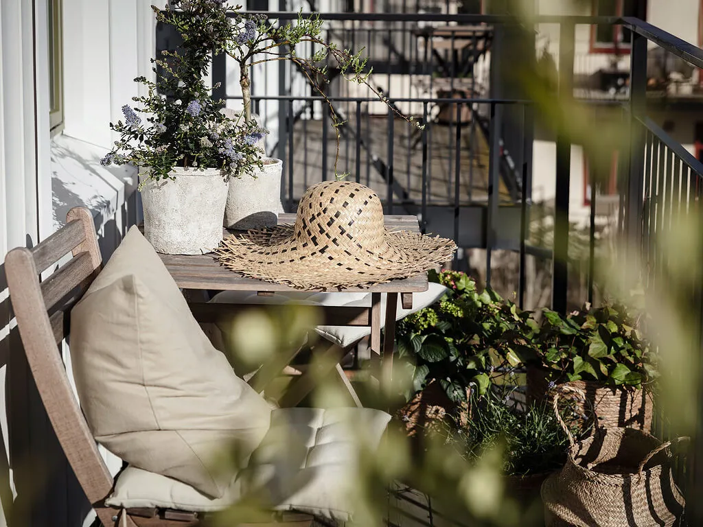 A cozy outdoor space featuring concrete planters, a woven basket, a wide-brimmed hat, and various potted plants.