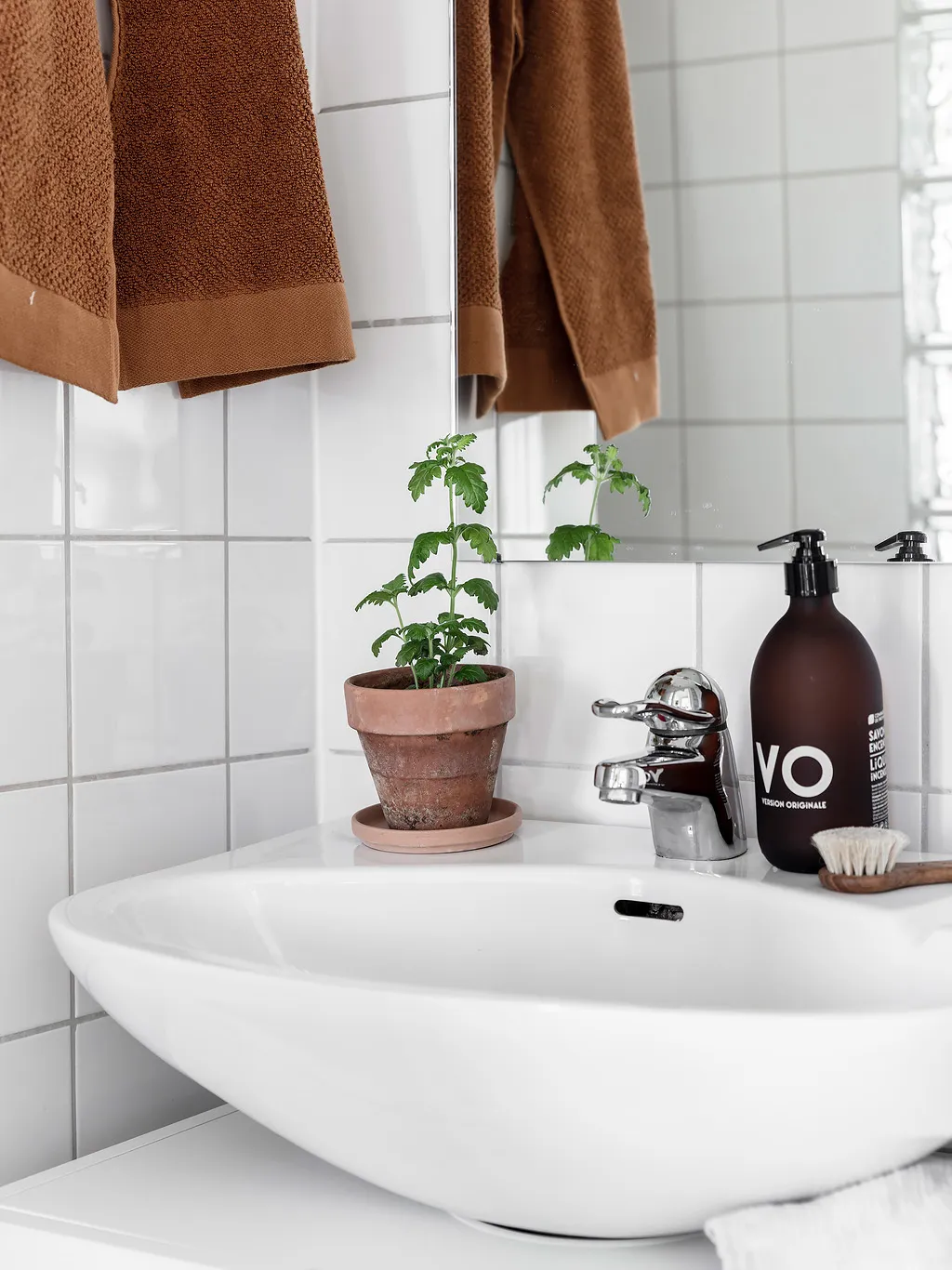 A minimalist bathroom with white tiles, a white sink, and a terracotta plant pot on the counter.
