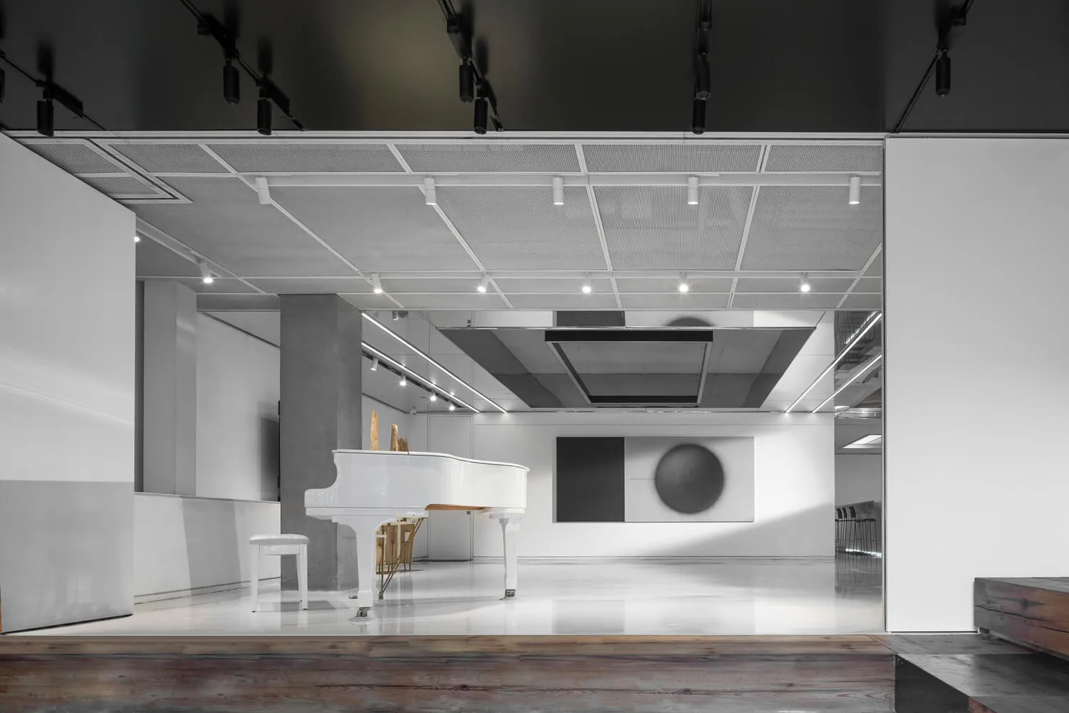 A minimalist room with a white piano and stool, featuring industrial-style lighting and a concrete pillar.
