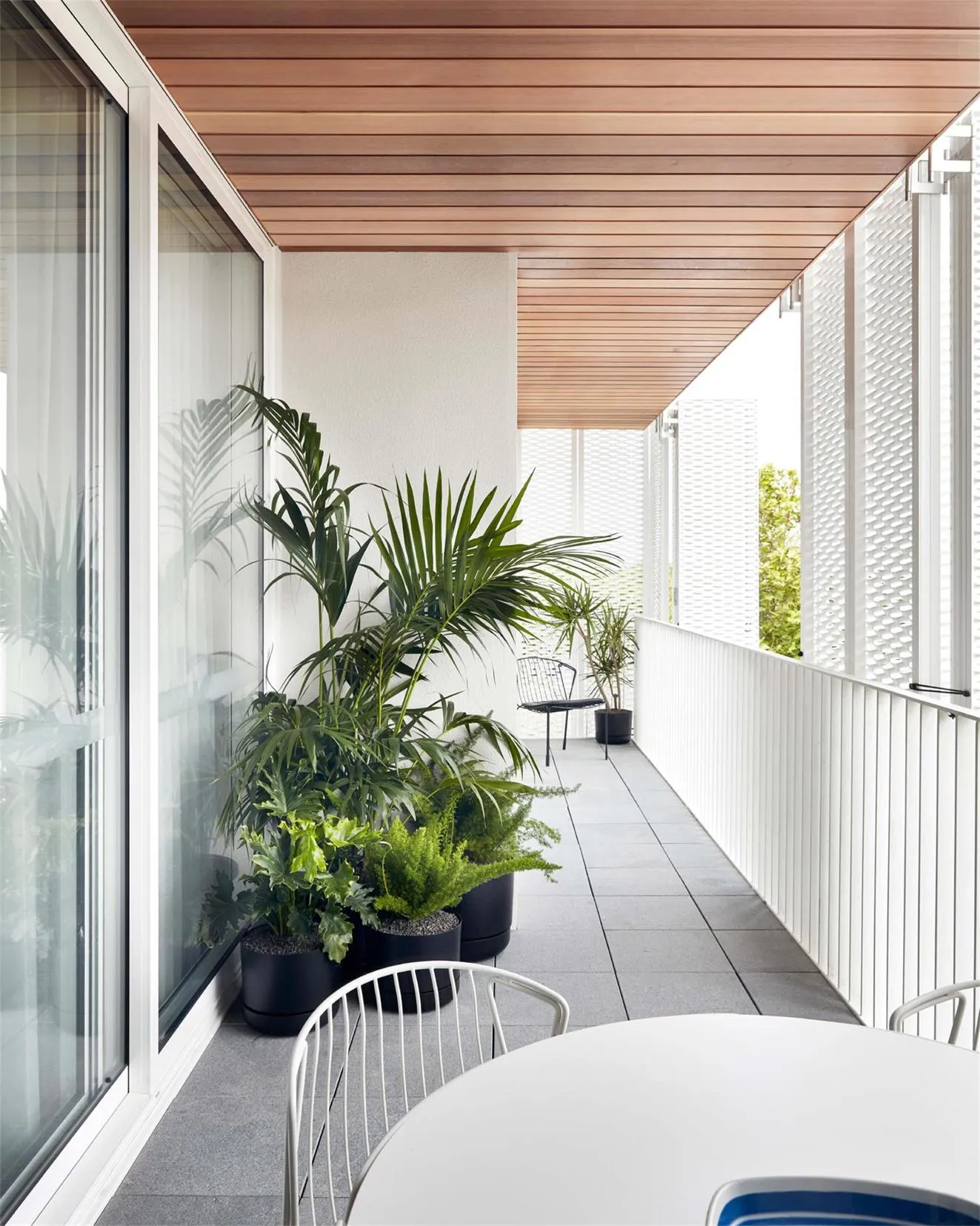 A modern balcony featuring sleek furniture, plants, and a minimalistic ceiling design, providing a relaxing outdoor living sp