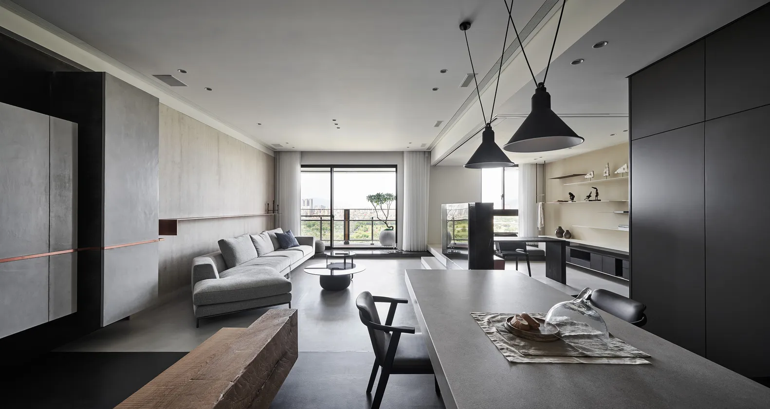 Modern, minimalist living room with concrete walls, a large sectional sofa, and a dining table with pendant lights.