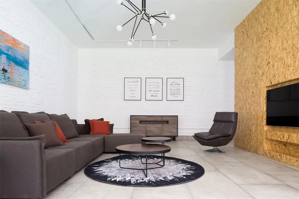 A modern living room with wooden walls, a gray sectional sofa, and a round coffee table on a patterned rug.