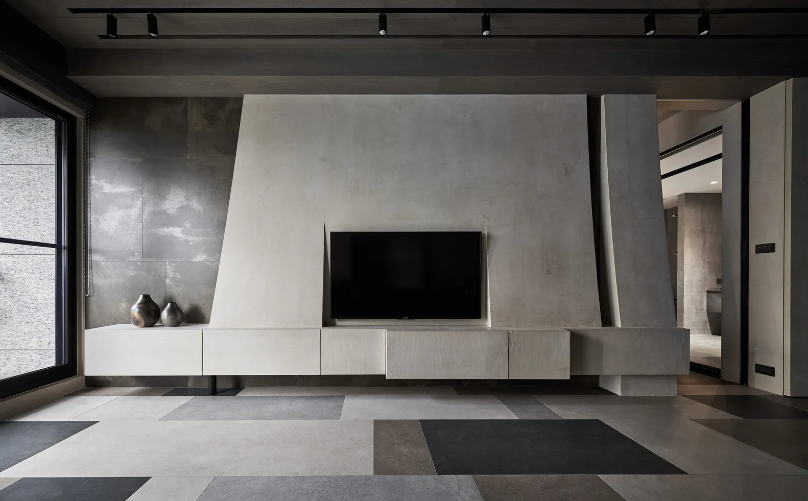 Modern minimalist living room with textured concrete walls and floor, featuring a sleek black flat-screen television.