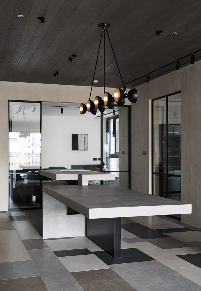 Contemporary office space featuring large concrete tables with black pendant lights hanging from a dark wooden ceiling.