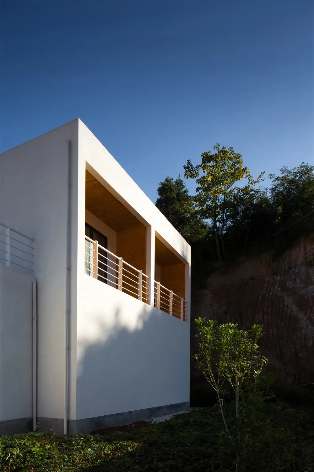 A modern, white residential house with wooden balconies and visible trees in the background.