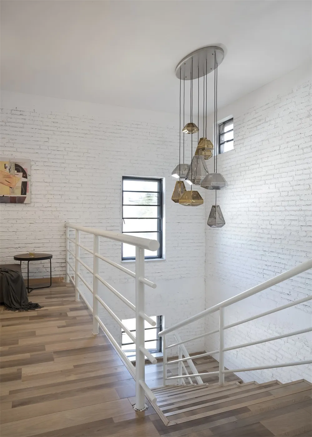 Modern interior staircase featuring brass lamps, white brick walls, and hardwood flooring.