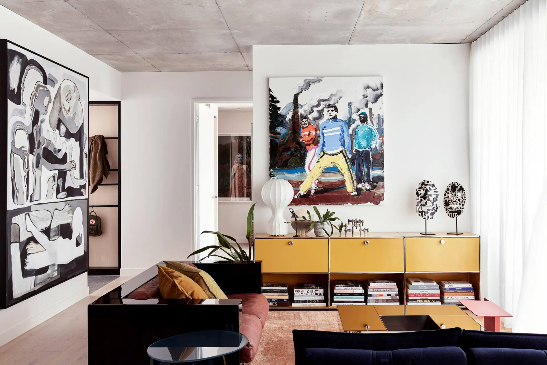 Contemporary living room featuring abstract artwork, yellow storage units, and a black couch with mustard-colored cushions.