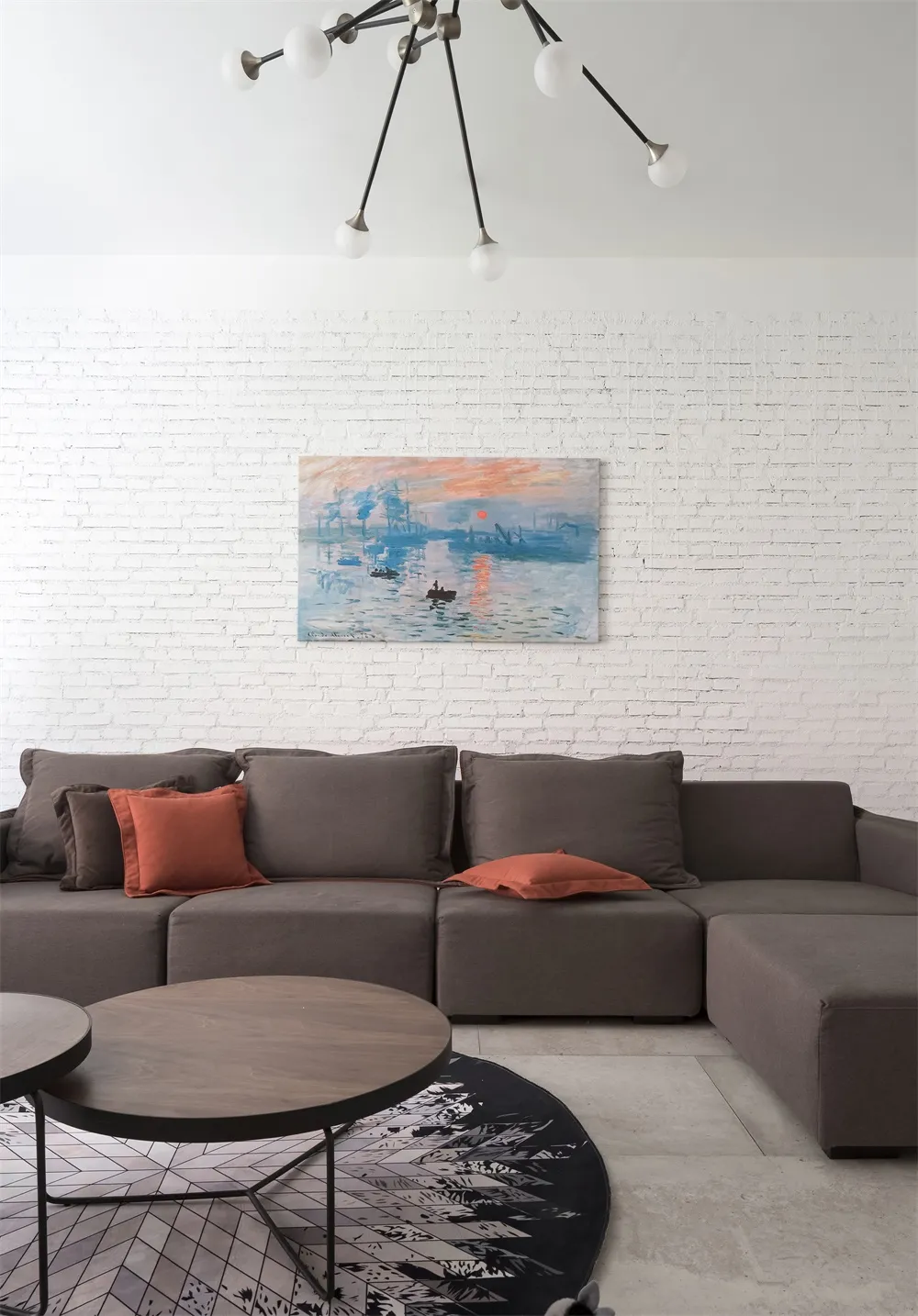 Modern living room featuring a grey sectional sofa, coffee table, and colorful artwork on a white brick wall.