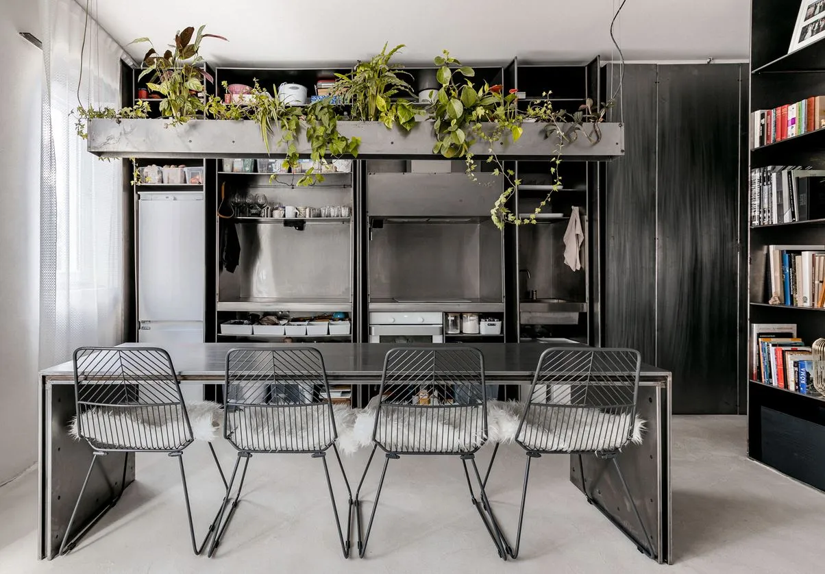 Modern urban housing unit with metal finishes, featuring a dining area with black metal chairs and table, and a kitchenette w