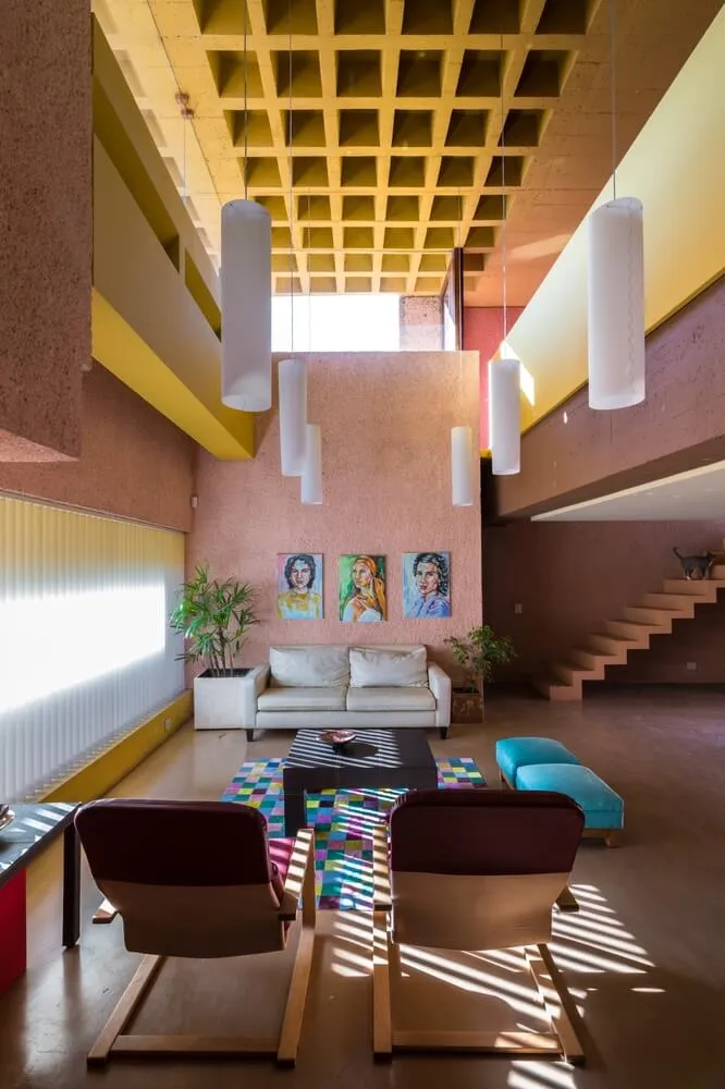 A modern living room with concrete walls and floors, featuring a white sofa, colorful rugs, hanging lamps, and a staircase in