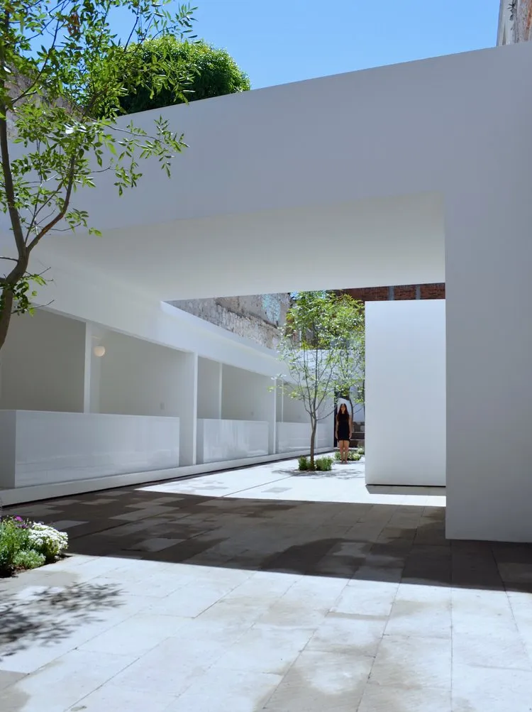 A modern pavilion with concrete walls and a glass roof, featuring a woman standing under an overhang.