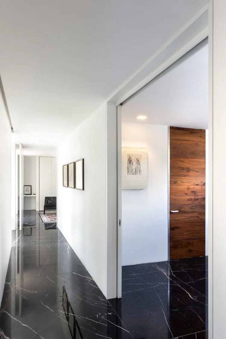 Modern minimalist hallway featuring black marble flooring and white walls.