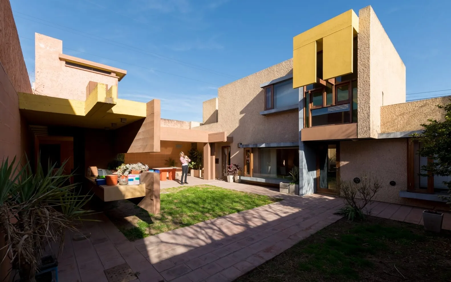A modern residential house with stucco exterior, featuring a courtyard and greenery.
