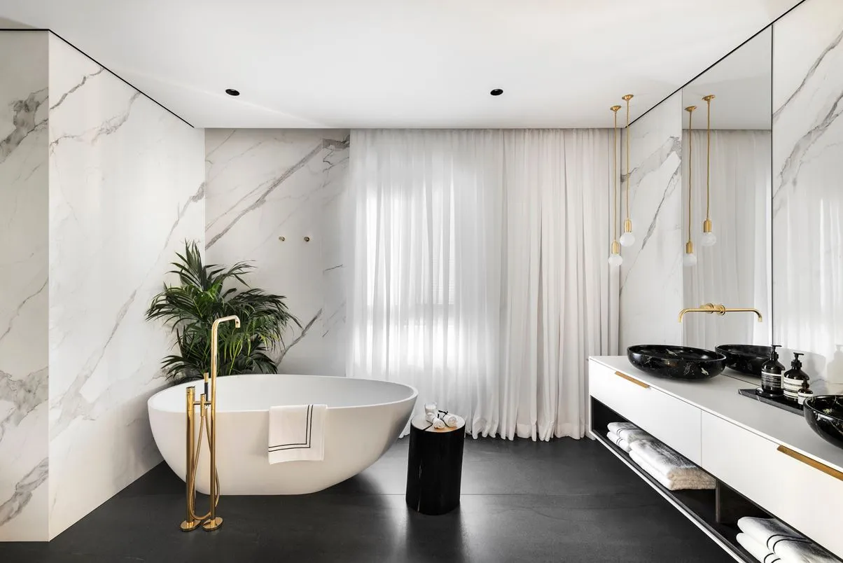 A minimalist bathroom featuring a freestanding bathtub, marble walls, and black accents.