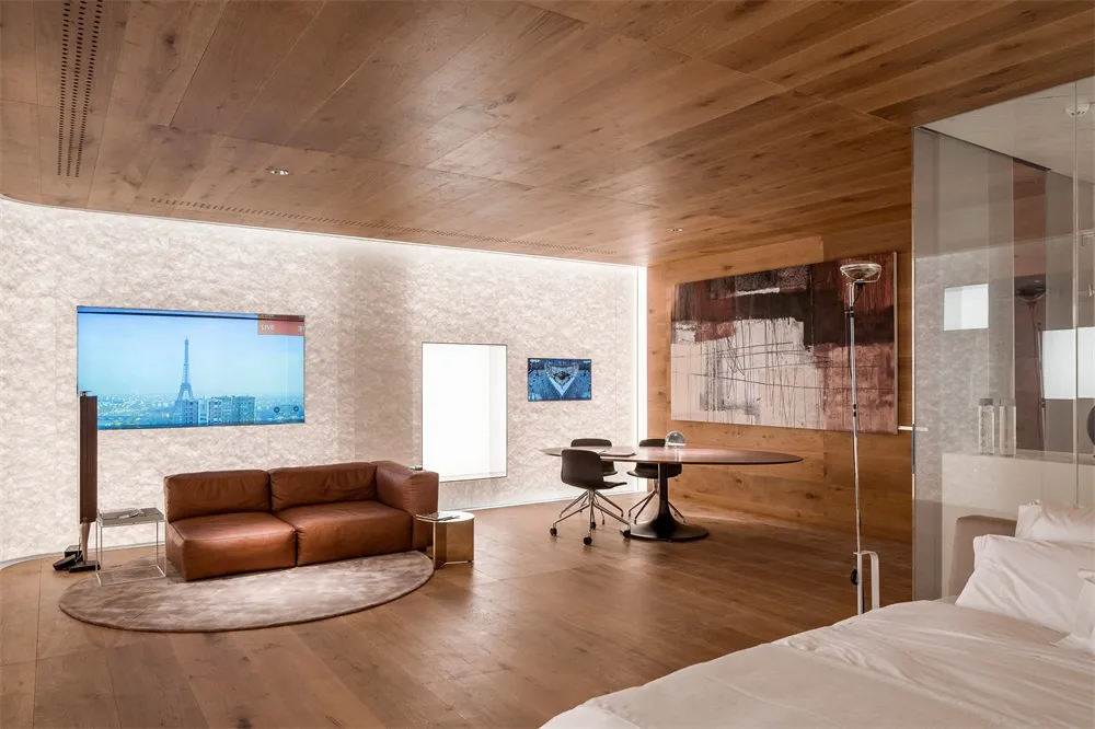 A modern bedroom with wooden flooring, a brown leather sofa, a round table, and a painting on the wall.