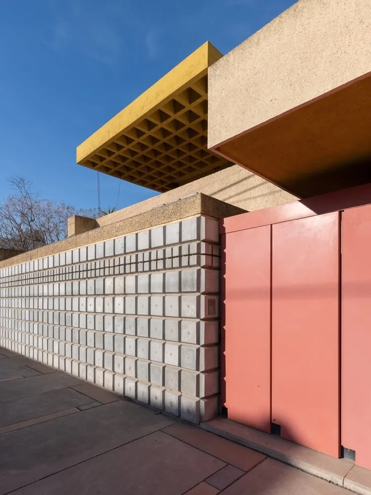 A modern building facade featuring a concrete wall and a red door.