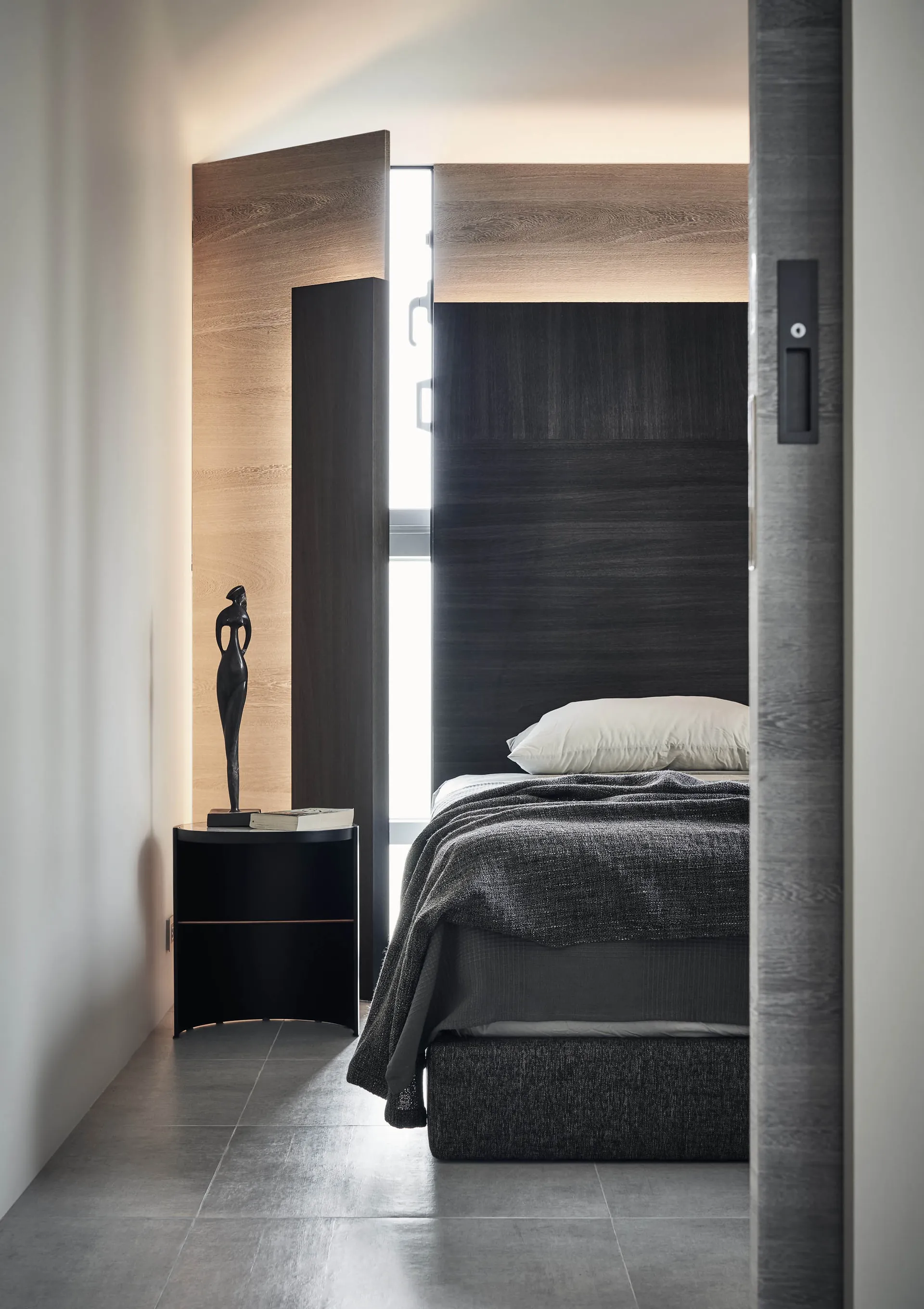 Modern minimalist bedroom with dark wood walls, a black bed frame, and a single sculpture on the nightstand.