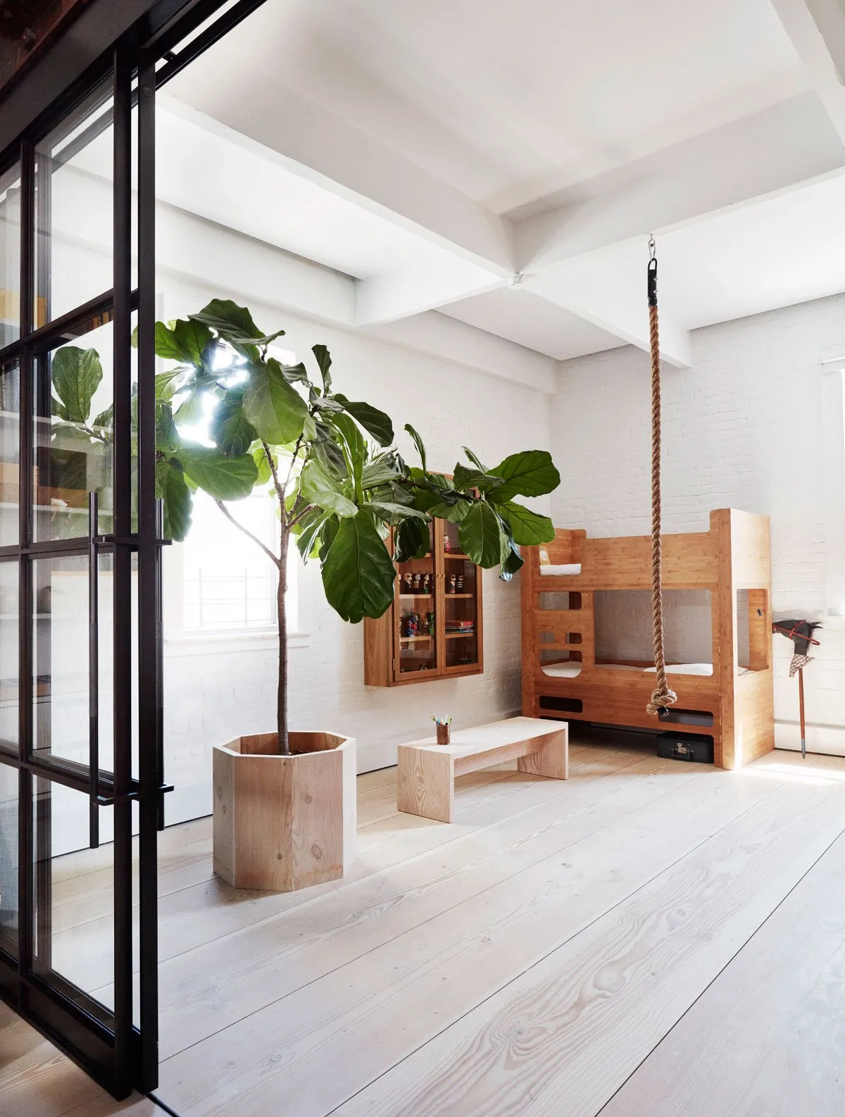 Industrial-style interior featuring a wooden swing bed suspended by a rope and a large fiddle leaf fig plant.