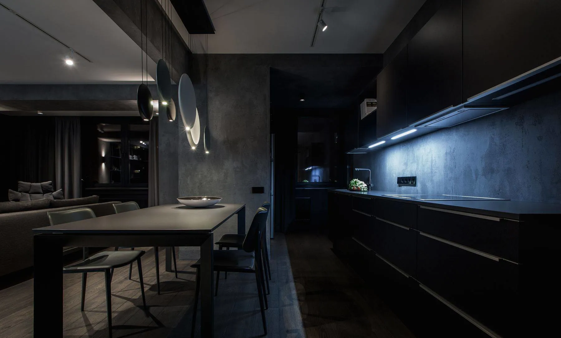 A modern residential kitchen with concrete walls and a black dining table with chairs.