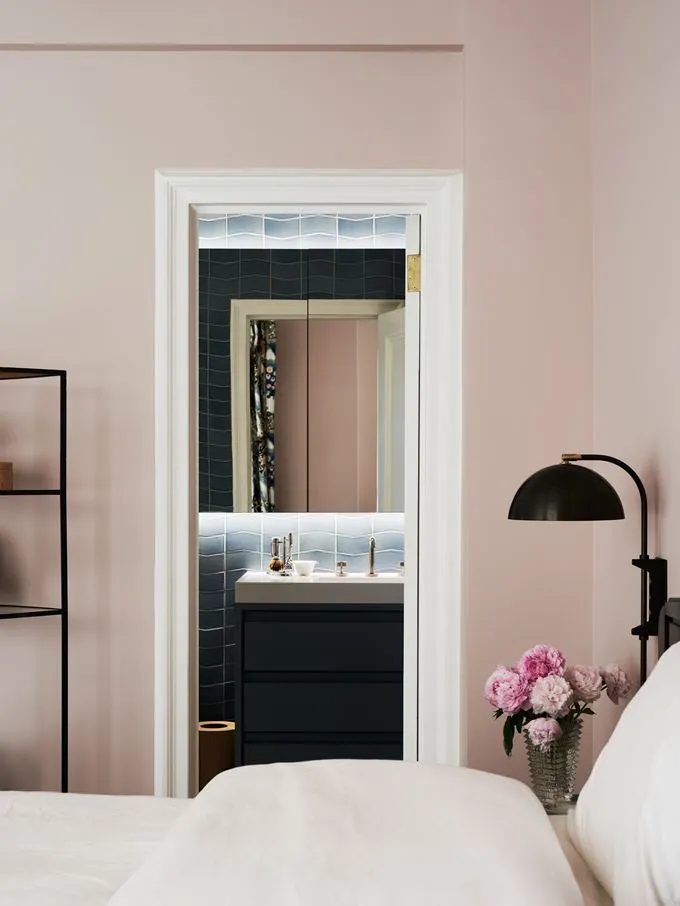 A minimalist bedroom with a pink wall, white furniture, and a mirror.