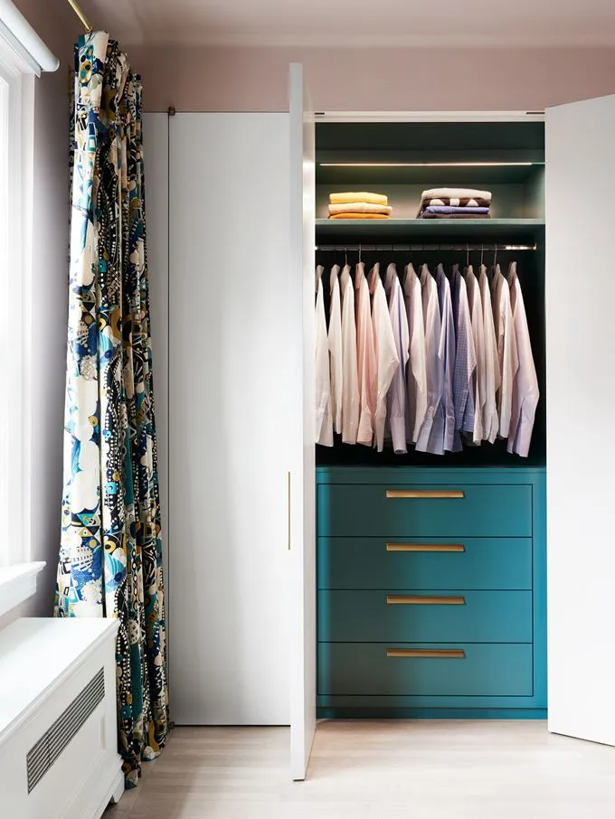 A minimalist closet with turquoise drawers and neatly arranged shirts on hangers.