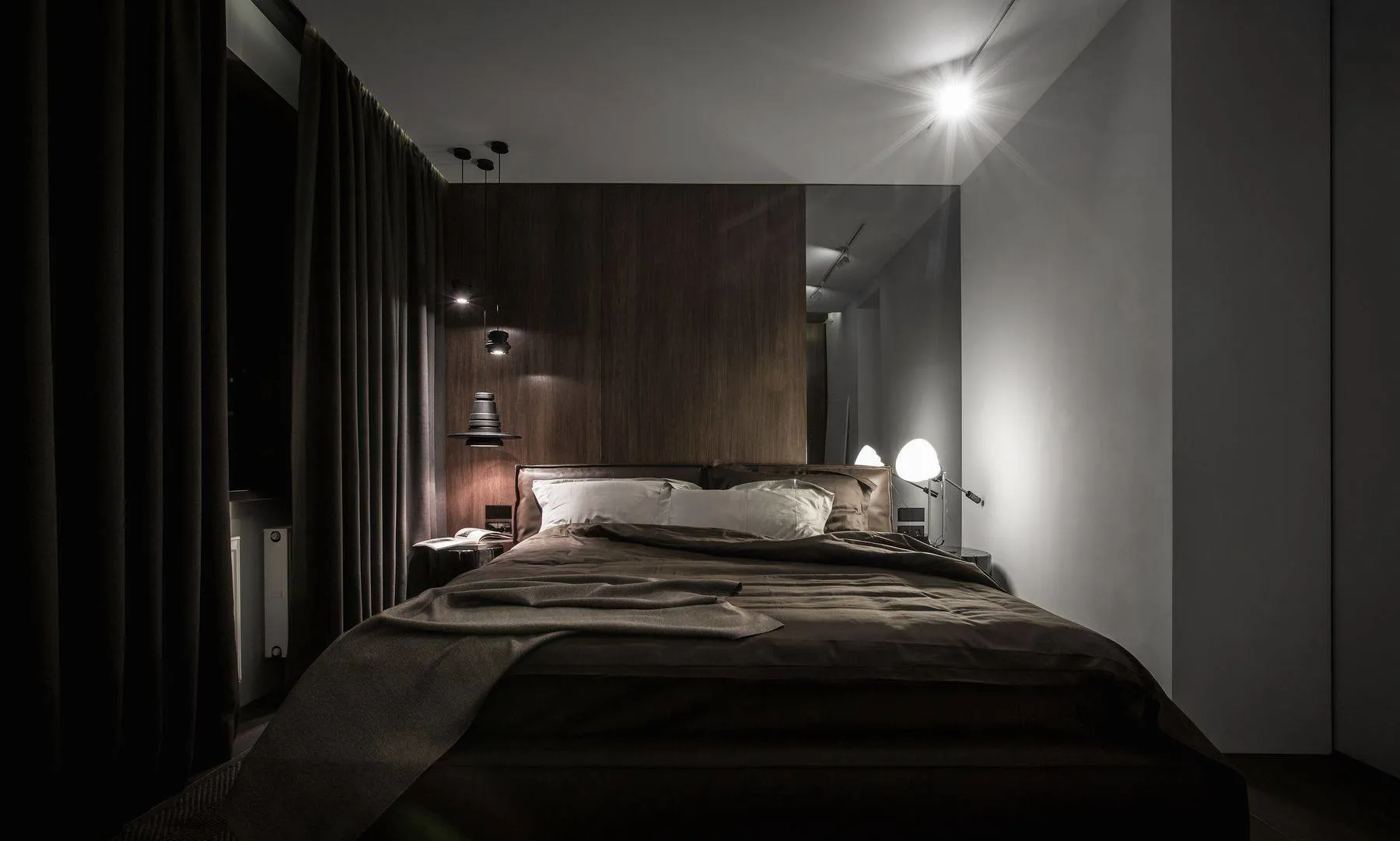 A modern bedroom featuring a wooden panel wall, a queen-sized bed with a dark comforter, and two bedside lamps.